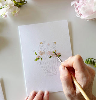 Hand painting a floral design on a white card with a brush.