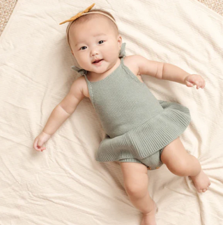 A baby girl lying on a swaddle in a sage green playsuit and headband