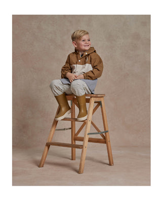 Little boy sitting on a ladder wearing Rylee & Cru's Boy's Raincoat with color blocking